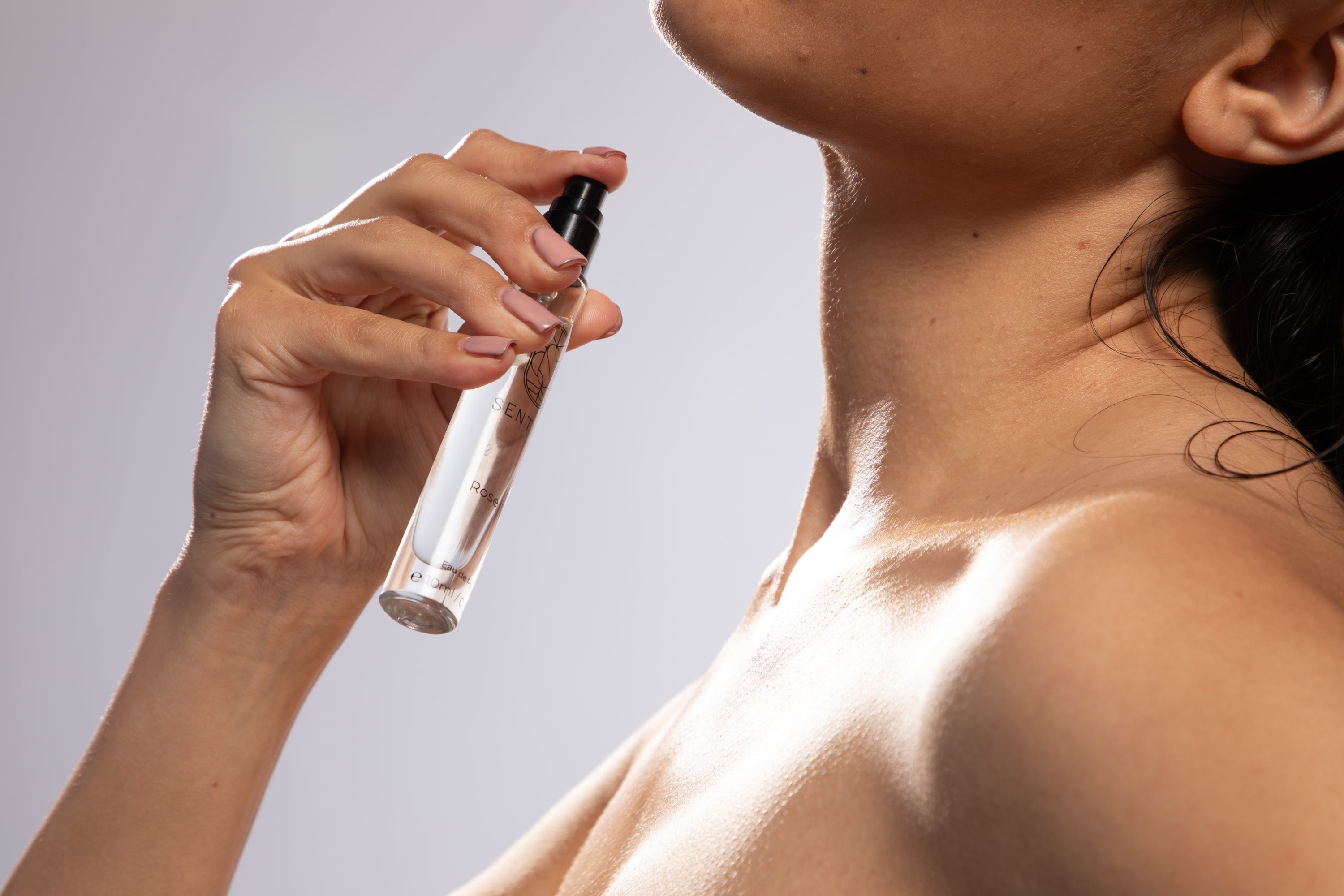 Person applying perfume to their neck against a neutral background

